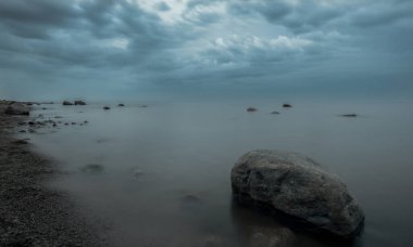 Büyük kayalıkları ve mavi sisi olan sisli bir sahil.