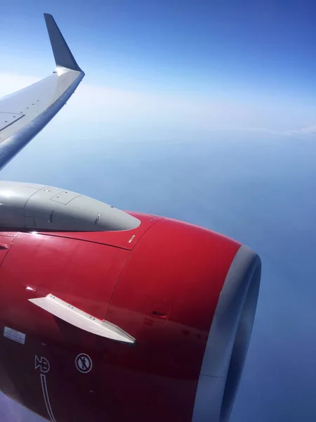 In the window of the plane, the turbine is red and the wing is in white clouds