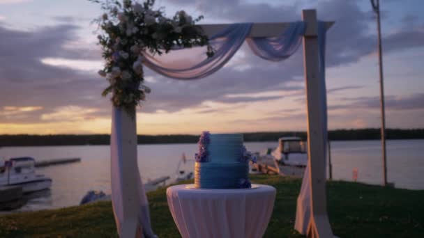 Gün batımında göl kenarında çok güzel bir düğün kemeri ve pasta. — Stok video