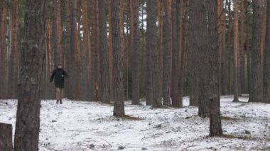Sırt çantalı bir adam kameranın yanındaki kış ormanında koşuyor.