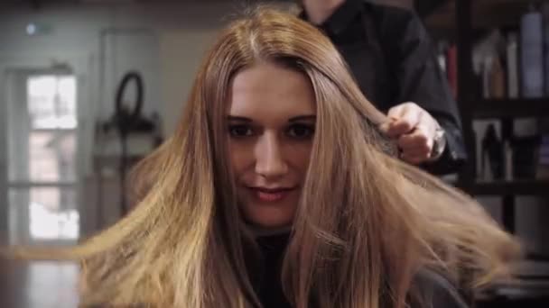 Дівчина посміхається в камеру, поки її волосся висушується в салоні — стокове відео