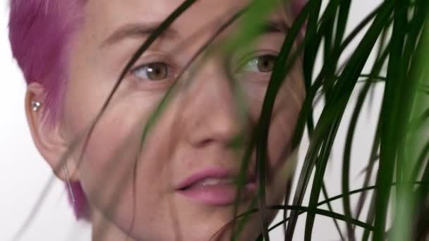 Лицо девушки с чистой кожей среди экзотических растений на белом фоне в студии — стоковое видео