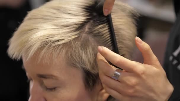 Egy fodrász egy fodrászszalonban ellenőrzi egy szőke lány hajhagymáját. — Stock videók