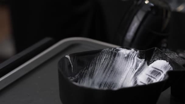 The hairdresser scoops white paint from a black bowl with a brush. Close up 4K — Stock Video