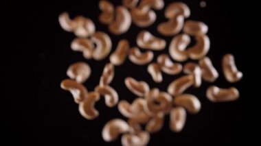 Kaju, siyah arka planda bir aşağı bir yukarı uçar. Kaju fıstıklı sağlıklı yemek pişirmek