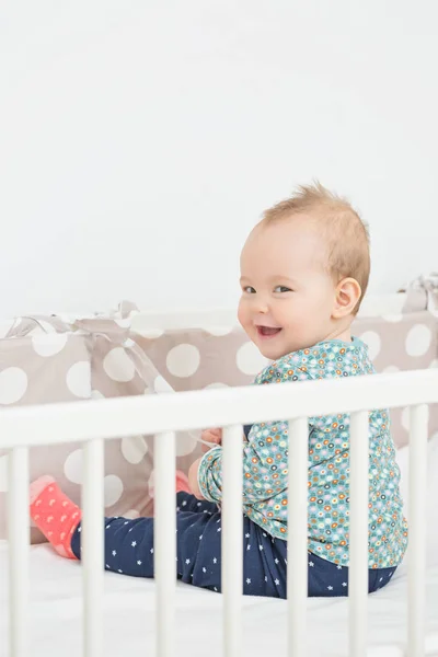 Acht Monate altes Mädchen sitzt lächelnd in ihrem Bett und schaut zu — Stockfoto