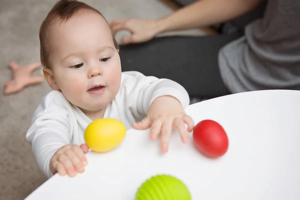 Nueve meses niña tratando de agarrar coloridos huevos de juguete — Foto de Stock
