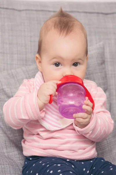 Bébé fille eau potable de la bouteille en plastique rouge — Photo
