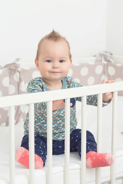 Acht Monate altes Mädchen sitzt lächelnd in ihrem Bett und schaut zu — Stockfoto