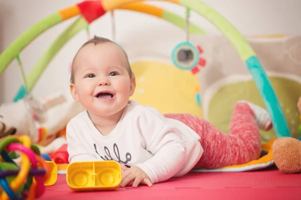 Osm měsíců starou holčičku hraje s barevnými hračkami na podlaze — Stock fotografie