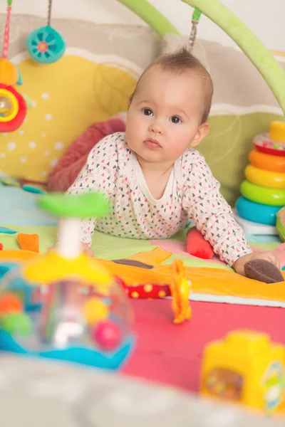 Osm měsíců starou holčičku hraje s barevnými hračkami na podlaze — Stock fotografie