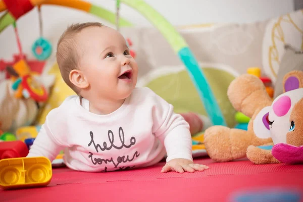Osm měsíců starou holčičku hraje s barevnými hračkami na podlaze Stock Snímky