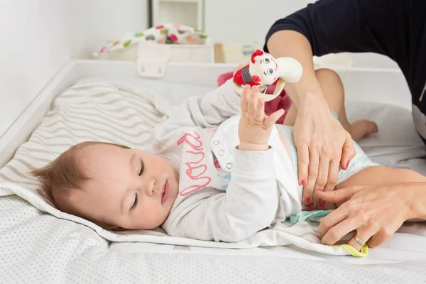 Mother changing diapers of a nine months old baby girl daughter Stock Photo