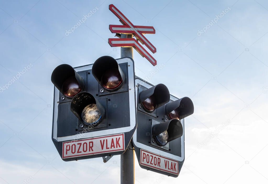 Railway traffic light with inscription ATTENTION TRAIN in Czech language under blue sky