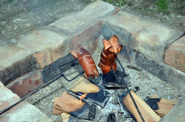 Duas salsichas grelhadas sobre um fogo na lareira de tijolo — Fotografia de Stock