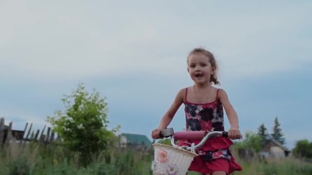 Drăguţă fetiţă care merge cu bicicleta la ţară. Zâmbește și își scoate limba — Videoclip de stoc