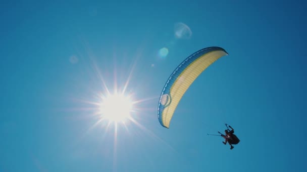 Parapente extremo volando contra un cielo azul claro, el rayo de sol brilla en la cámara — Vídeo de stock