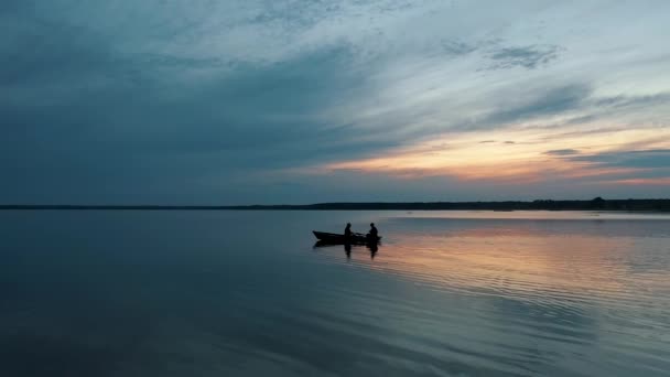 Silhouetten zweier Fischer, die bei Sonnenuntergang auf einem kleinen Boot segeln — Stockvideo