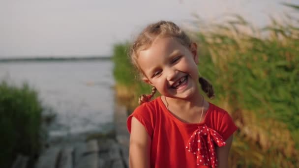 Портрет милой маленькой девочки смотрит в камеру и улыбается на открытом воздухе — стоковое видео