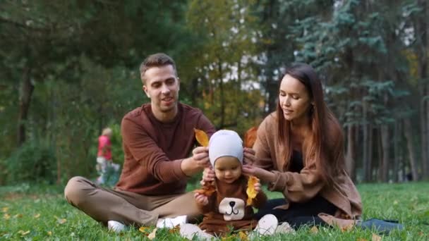 Young mother, father and little son play with leaves in autumn park — Stock Video