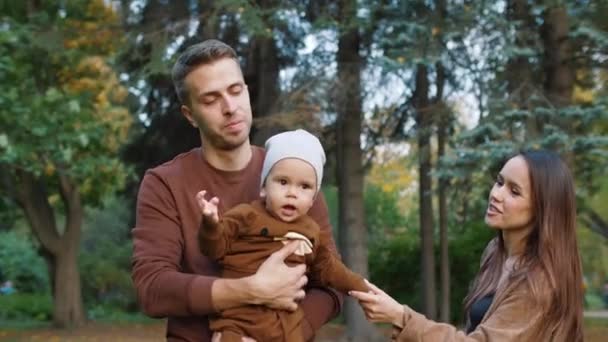 Мати і батько тримають маленьку дитину в руках і цілують його з обох сторін — стокове відео