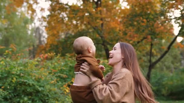 Boldog fiatal anya feldobja aranyos vidám kisfiát a levegőbe a parkban — Stock videók