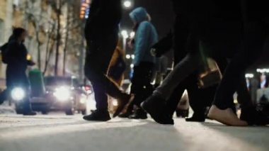 Crowd of pedestrians crossing busy city street at night, slow motion.