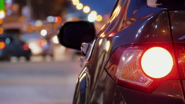 Atrás del coche estacionado en el fondo del tráfico de coches de la ciudad, luces traseras del coche están encendidas — Vídeo de stock