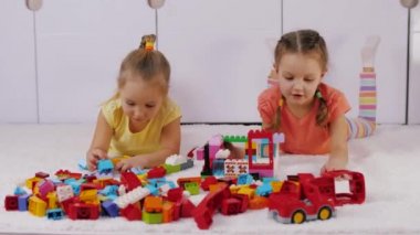Little girls lie on carpet and assemble house of lego plastic building bricks