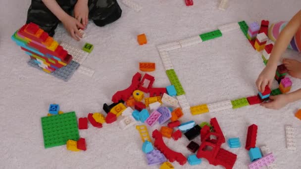 Дети играют в красочного пластикового конструктора, сидящего на ковре в детском саду — стоковое видео