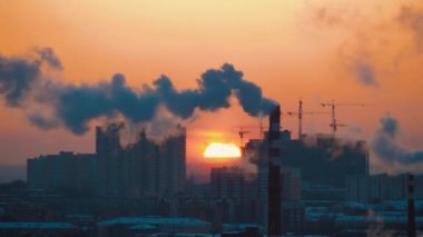 Sun sets behind apartment, multi-story buildings, smoking chimneys pollutes air