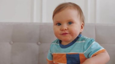 Adorable happy little boy with blue eyes smiles and rejoices at home, close up