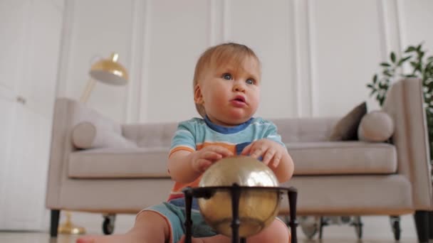 Adorable baby boy blue eyed is sitting on floor at home, playing with toy globe — Αρχείο Βίντεο