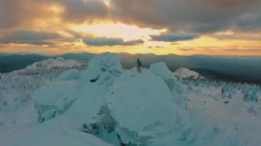 Aerial: hiker standing on top of snowy mountain at beautiful winter sunset