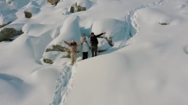 Aerial dronie shot: hikers waving hands standing on snow covered mountain slope