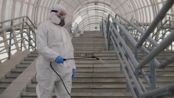 Virologo in tuta protettiva disinfetta la superficie, spruzza prodotti chimici su corrimano — Video Stock