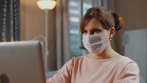 Женщина в медицинской маске работает удаленно от дома, самоизоляция — стоковое видео