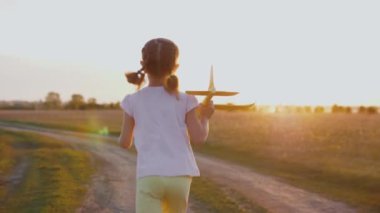 Mutlu küçük kız gün batımında oyuncak uçakla tarlada koşuyor.