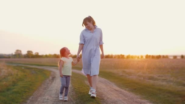 Мама гуляет с маленькой дочерью на золотом закате, весело провести время, улыбается и счастлив — стоковое видео