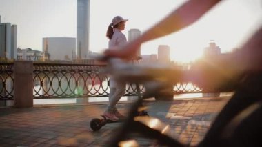 Pembe ceketli çekici bir kadın gezinti güvertesinde elektrikli scooter kullanıyor.
