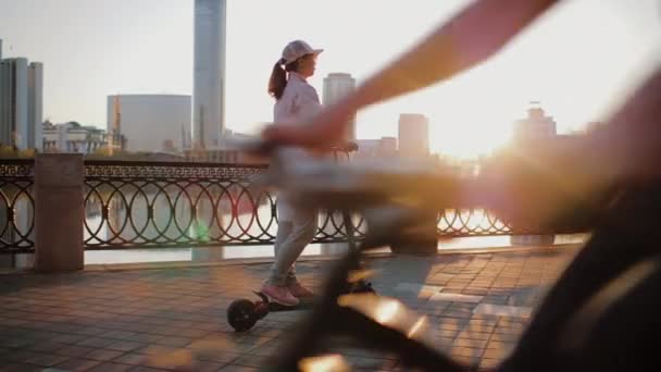 Приваблива жінка, одягнена в рожеву куртку, їде на електричному скутері на набережній — стокове відео