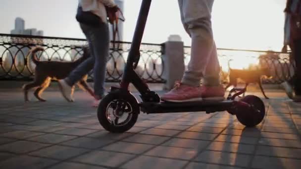 Pernas de menina se move em scooter elétrico no calçadão da cidade durante o pôr do sol — Vídeo de Stock