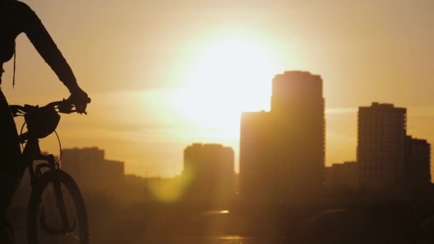 Silueta de dos ciclistas montados sobre el fondo de edificios urbanos durante la puesta del sol — Vídeos de Stock