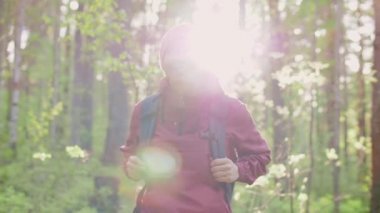 Sırt çantalı gülen bir yürüyüşçü patika boyunca yürür, vahşi ormana bakar.