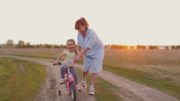 Mom teaches little daughter to ride bike at sunset outdoors nature — Stock Video
