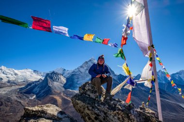 Nangkarsang Tepesi 'ndeki kayalıklarda oturan Asyalı yürüyüşçü, Everest Ana Kampı, açık mavi gökyüzü ve Himalaya sıradağları arka planda..