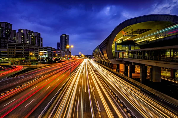 Sendero ligero de tráfico concurrido con la estación de tren LRT, edificios de oficinas y cielo azul oscuro al fondo en Puchong, Malasia . — Foto de Stock