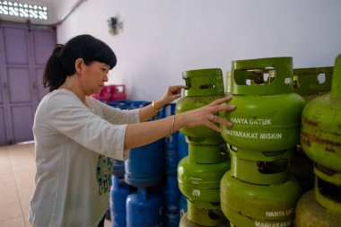 Endonezyalı kadınlar yerel bir işletme olan Warung 'da 3 kiloluk gaz tüpleri düzenliyorlar. Metnin çevirisi 'sadece fakirler için'. Seçici Odaklanma.