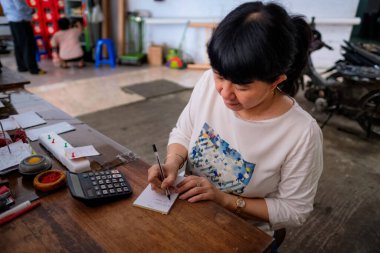 Asyalı Endonezyalı kadınlar, küçük yerel bir aile işletmesi sahibi, ya da yerel olarak Warung olarak adlandırılan, masasının kârını hesaplayan. Seçici Odaklanma.