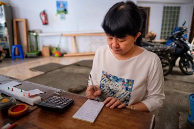 Asyalı Endonezyalı kadınlar, küçük yerel bir aile işletmesi sahibi, ya da yerel olarak Warung olarak adlandırılan, masasının kârını hesaplayan. Seçici Odaklanma.